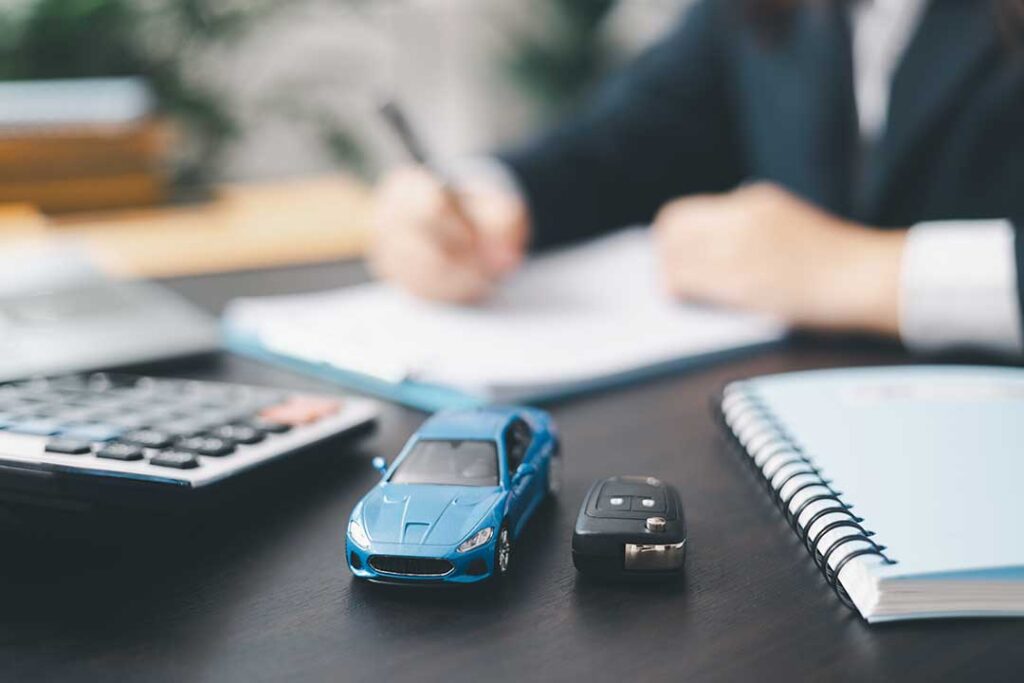 A person browsing car listings on a laptop at a kitchen table, notebook and coffee mug nearby.