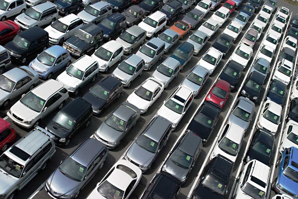 A person reviewing a checklist while speaking with a car dealer next to several parked vehicles.