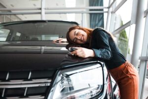 A buyer reviews an auto loan worksheet beside a parked vehicle with a calculator and pen.